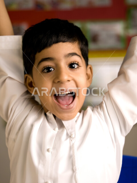 الاستعداد للعام الدراسي الجديد، المدارس الأكاديمية في الإمارات العربية المتحدة، صورة مقربة لطالب عربي خليجي إماراتي يرتدي الكندورة يرفع يديه عاليا، ايماءات وجه ويدين تدل على الحماس والسعادة بالعودة إلى المدرسة.