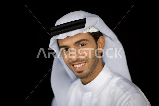 الاهتمام بالمظهر الخارجي، التقاط صورة شخصية للوثائق الرسمية, بورتريه مقرب لرجل عربي خليجي إماراتي مبتسم يرتدي الكندورة والغترة ينظر إلى الكاميرا بإيماءت السرور والثقة, خلفية سوداء