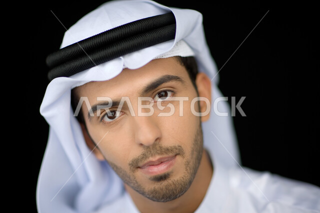 ايماءات الجدية والثقة, التقاط صورة شخصية للوثائق الرسمية, الاهتمام بالمظهر الخارجي, بورتريه مقرب لشاب عربي خليجي إماراتي يرتدي الكندورة والغترة ينظر إلى الكاميرا, خلفية سوداء
