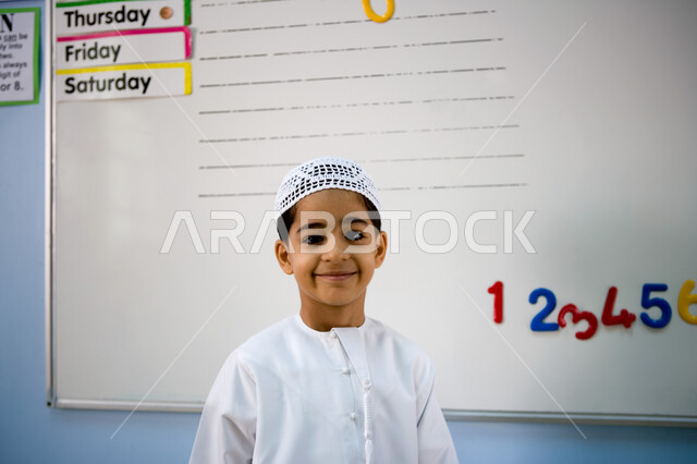 Arithmetic activities and the development of intelligence among boys, the objectives of education in the schools of the United Arab Emirates, a smiling Emirati Gulf Arab student wearing a white cap and an Emirati kandora standing in front of the board, ba