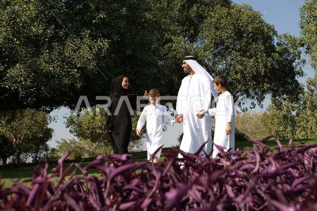 استغلال وقت الفراغ في التسلية والمرح والترفيه، الذهاب إلى الحديقة مع الأسرة في يوم العطلة الاسبوعية، صورة مقربة لعائلة عربية خليجية إماراتية ترتدي الزي الإماراتي التقليدي تقوم بالمشي على العشب في الحدائق والمرافق العامة، قضاء أوقات عائلية ممتعة مع الأبناء