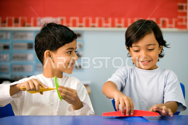 أهمية تعلم مهارة التركيز والابتكار لدى الطلاب، صورة مقربة لتلميذين عربيين خليجين اماراتيين يرتديان اليونيفورم الاماراتي ويمسكان البوصلة، التعلم عن طريق اللعب داخل الفصل، الاستمتاع بالنشاطات الجماعية الترفيهيه في المدارس