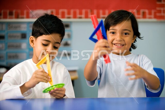 النشاطات الجماعية الترفيهيه في المدارس، أهمية تعلم مهارة التركيز والابتكار لدى الطلاب، صورة مقربة لتلميذين عربيين خليجين اماراتيين يرتديان اليونيفورم الاماراتي ويمسكان البوصلة، التعلم عن طريق اللعب داخل الفصل