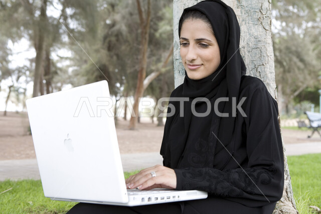 Green nature background, completing work tasks, professionalizing computer and information technology jobs, a veiled Arab Emirati woman using a laptop, using modern technical devices, surfing the Internet, sitting outdoors, a remote work session