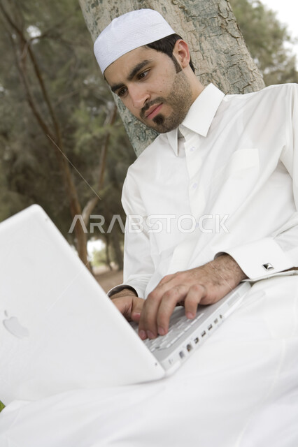 Completing work tasks, professionalizing computer and information technology jobs, a Saudi Arabian Gulf man using a laptop, using modern technical equipment, surfing the Internet, sitting outdoors, green nature, a remote work session