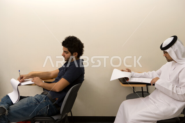 طالبان جامعيان عربيان خليجيان إماراتيان في قاعة المحاضرات في الجامعة، ورش عمل ودورات تدريبية في الإمارات، قراءة الكتب وكتابة وتدوين الملاحظات المهمة أثناء شرح المحاضرة، التعليم العالي في الجامعات والكليات الأكاديمية الإماراتية