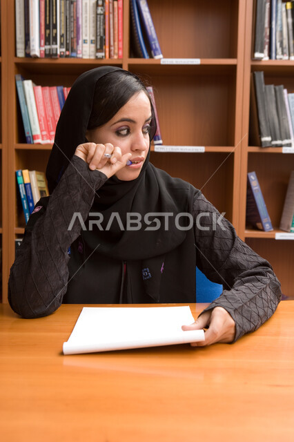 البحث والتفكير في المواد الدراسية، طالبة إماراتية عربية خليجية تجلس في مكتبة الجامعة، الدراسة في مكتبة الجامعة وتدوين وكتابة التقارير، تنمية الأفكار واكتساب المعلومات، التعليم العالي في الجامعات والكليات الأكاديمية الإماراتية