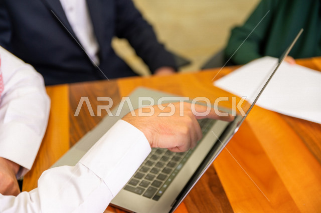 اجتماع اداري مع مجموعة من الأشخاص السعوديين الخليجيين في غرفة الاجتماعات  ، اجتماع رجال اعمال و سيده اعمال سويا داخل الشركة ، استخدام الكمبيوتر المحمول لادارة الاعمال ،  شركة سعودية ، عمل خليجي ،  فريق العمل 
