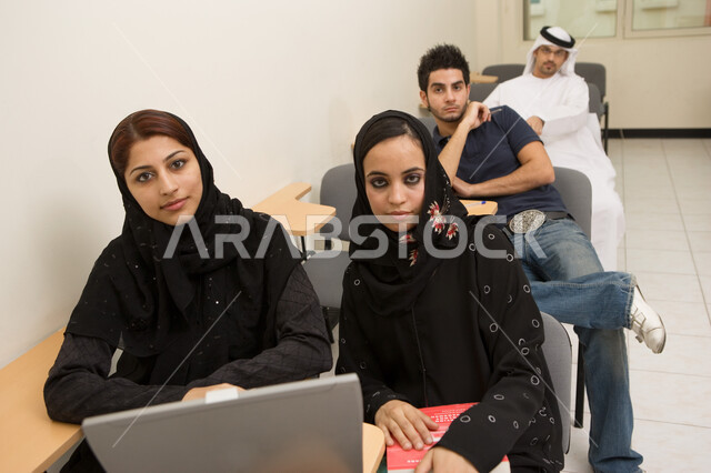 Diversifying and developing university education methods in the Emirates, a close-up of two Arab Gulf Emirati students using a laptop in education, a group of Emirati students in the lecture hall, workshops and training courses, attention, focus and liste