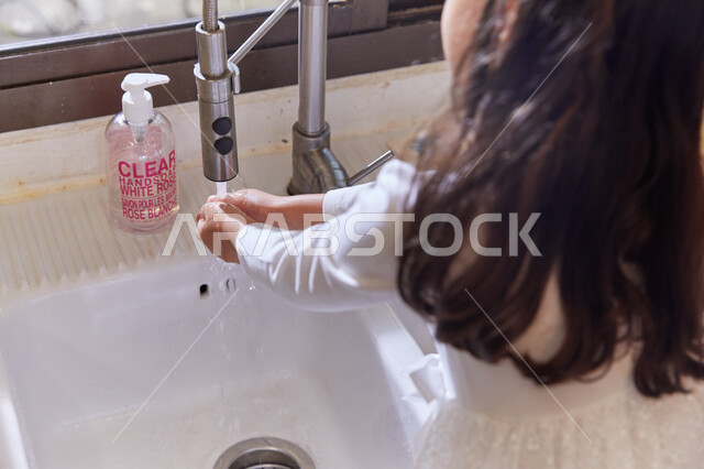 الإهتمام والعناية بالنظافة الشخصية، إتباع الإجراءات الوقائية للحمايه من الجراثيم والميكروبات، صوره من الخلف لطفله عربيه خليجيه اماراتية تقف أمام المغسلة وتقوم بغسل يديها جيدا بالماء والصابون، الرعايه الصحيه والوقايه من فايروس كورونا.