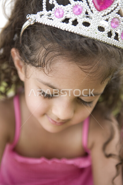 الاهتمام بالانوثة و الاناقة منذ الصغر, تعزيز الثقة بالنفس وتقوية الشخصية للاطفال, تقمص وتقليد شخصيات الاميرات الكرتونية, صورة مقربة لفتاة صغيرة عربية خليجية إماراتية ترتدي فستان وتاج الأميرة  في إحدى الحدائق العامة