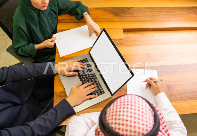 اجتماع اداري مع مجموعة من الأشخاص السعوديين الخليجيين في غرفة الاجتماعات  ، اجتماع رجال اعمال و سيده اعمال سويا داخل الشركة ، استخدام الكمبيوتر المحمول لادارة الاعمال ،  شركة سعودية ، عمل خليجي ،  فريق العمل 