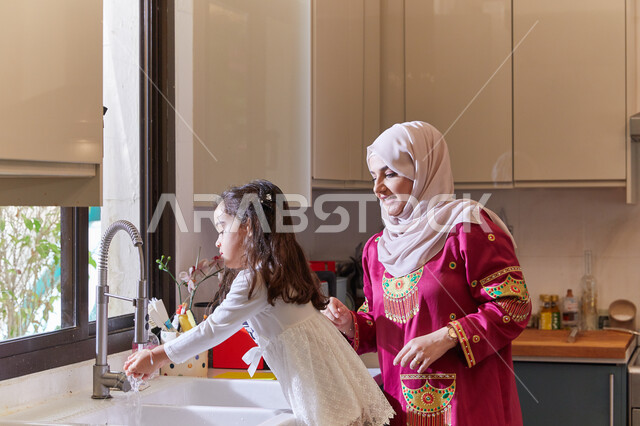 المساعده في تنظيف وغسيل الأطباق، الإستمتاع بأداء الأعمال المنزليه برفقة الأبناء، أم عربية خليجية اماراتية  تقف مع ابنتها في المطبخ، انجاز المهام الروتينيه في المنزل، تربيه الأطفال على حب التعاون.