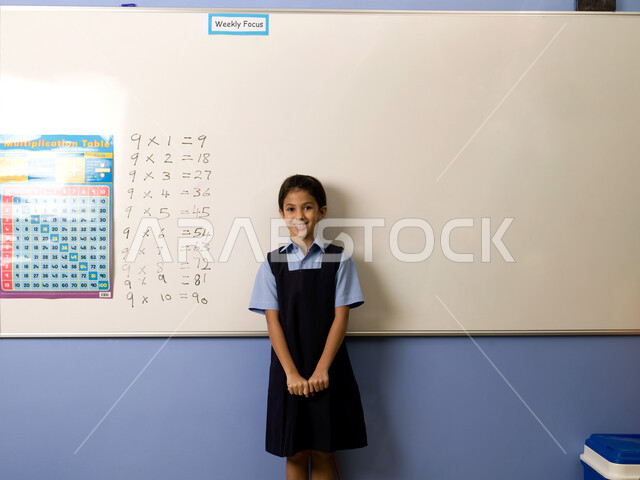 تنمية القدرات الفكرية ومهارات الحساب لتلاميذ المرحلة الابتدائية، تعلم جدول الضرب والعمليات الحسابية في الرياضيات، جودة التعليم في مدارس الإمارات العربية المتحدة، تلميذة عربية خليجية إماراتية ترتدي الزي المدرسي تقف بإيماءات الثقة بالحل الصحيح.