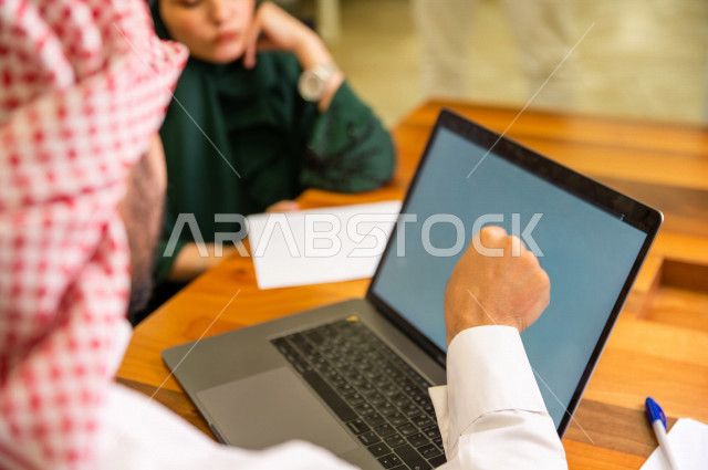 Administrative meeting with a group of Saudi Gulf people in the conference room, meeting of businessmen and a businesswoman together inside the company, using a laptop computer to manage a business, a Saudi company, Gulf work, work team