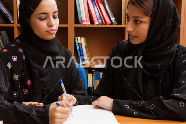 مفهوم التعاون ومشاركة الزملاء في الدراسة، طالبتان عربيتان خليجيتان إماريتيان تقضيان الوقت بقراءة ومراجعة الدروس اليومية في مكتبة الجامعة، تدوين الملاحظات وكتابة التقارير والأبحاث العلمية، تنمية المهارات الذهنية، الجامعات والكليات الإماراتية