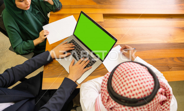 اجتماع اداري مع مجموعة من الأشخاص السعوديين الخليجيين في غرفة الاجتماعات  ، اجتماع رجال اعمال و سيده اعمال سويا داخل الشركة ، استخدام الكمبيوتر المحمول  بخلفية خضراء كروما  لادارة الاعمال ،  شركة سعودية ، عمل خليجي ،  فريق العمل 