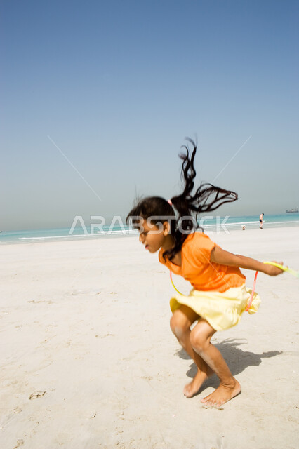 أنشطة ترفيهية صيفية في العطلة, الإستمتاع بالفعاليات الصيفية الممتعة , فتاة صغيرة عربية إمراتية خليجية تقوم باللعب على شاطئ البحر وتستمتع بالقفز على الحبل, منتجعات شاطئية في الإمارات