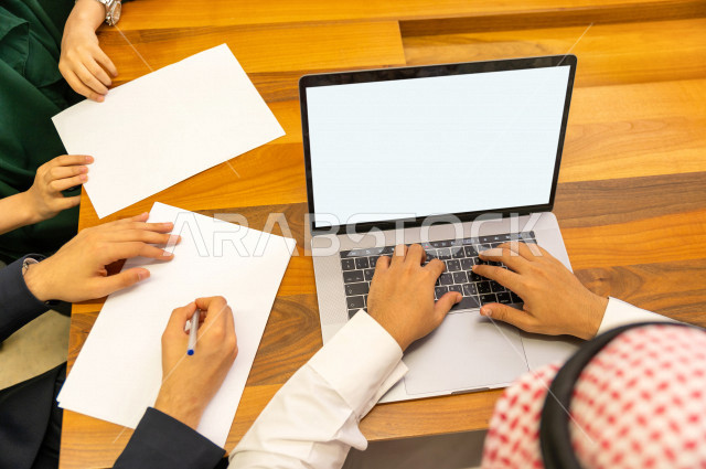 اجتماع اداري مع مجموعة من الأشخاص السعوديين الخليجيين في غرفة الاجتماعات  ، اجتماع رجال اعمال و سيده اعمال سويا داخل الشركة ، استخدام الكمبيوتر المحمول لادارة الاعمال ،  شركة سعودية ، عمل خليجي ،  فريق العمل 