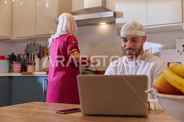 متابعة أخبار مواقع التواصل الاجتماعي، قضاء أوقات ممتعه في المطبخ، رجل عربي خليجي اماراتي يرتدي الكندوره والطاقية الاماراتيه يقوم بالعمل أونلاين عبر الحاسوب، امرأه عربيه خليجيه اماراتيه محجبه ترتدي عباءه مطرزه تقوم بتحضير الطعام، إجراء مكالمات الفيديو.