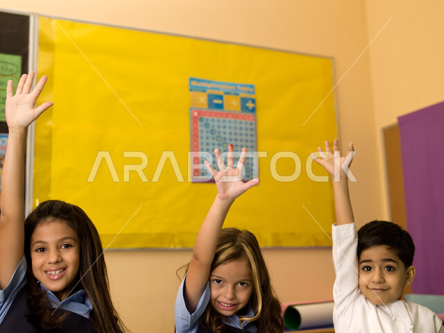 الحماس والتفاعل والمشاركة مع المعلمة برفع اليد، الالتزام والانضباط بقواعد الفصل المدرسي، صورة مقربة لتلاميذ عرب خليجيين إماراتيين يرتدون الزي المدرسي الإماراتي يرفعون أيديهم عاليا، المدارس التعليمية في الإمارات العربية المتحدة.