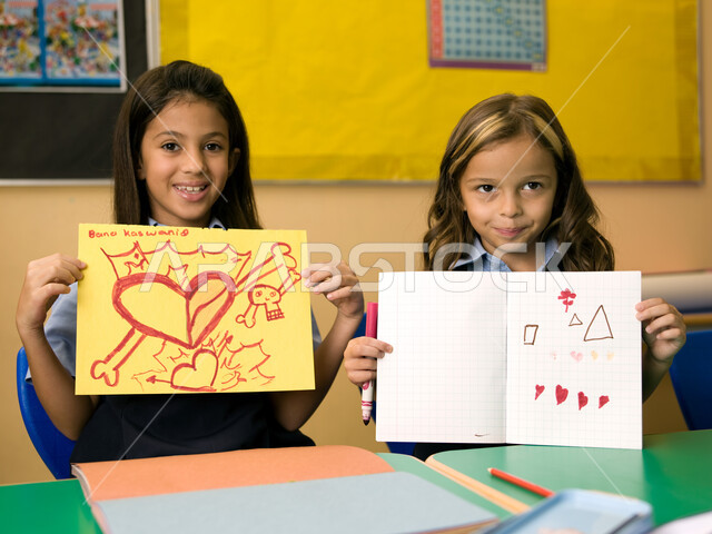 التعبير بالرسم عن مشاعر الحب والمودة، القرطاسية وأدوات التلوين، طالبتان عربيتان خليجيتان إماراتيتان ترتديان الزي المدرسي وتقومان بعرض الرسومات، المدارس التعليمية في الإمارات العربية المتحدة، ايماءات تدل على السعادة والفرح بالإنجاز.