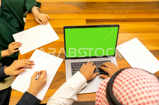 اجتماع اداري مع مجموعة من الأشخاص السعوديين الخليجيين في غرفة الاجتماعات  ، اجتماع رجال اعمال و سيده اعمال سويا داخل الشركة ، استخدام الكمبيوتر المحمول  بخلفية خضراء كروما  لادارة الاعمال ،  شركة سعودية ، عمل خليجي ،  فريق العمل 