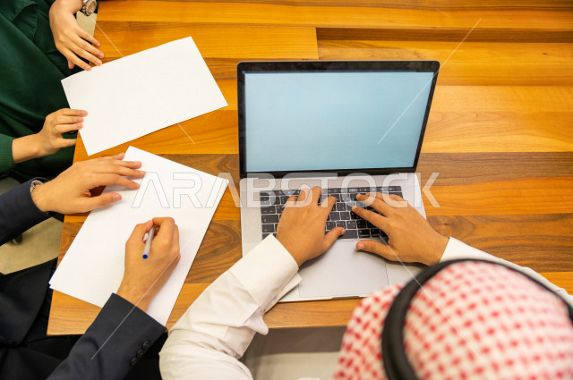 اجتماع اداري مع مجموعة من الأشخاص السعوديين الخليجيين في غرفة الاجتماعات  ، اجتماع رجال اعمال و سيده اعمال سويا داخل الشركة ، استخدام الكمبيوتر المحمول لادارة الاعمال ،  شركة سعودية ، عمل خليجي ،  فريق العمل 