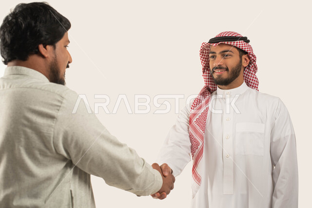 السلام والتحية والاتفاق على انجاز المهام, بورتريه مقرب لشاب عربي خليجي سعودي مبتسم يرتدي الثوب والشماغ يصافح رجل سعودي, مهن ووظائف سعودية, الحرف اليدوية التقليدية, التعارف وبناء العلاقات الاجتماعية, خلفية بيضاء
