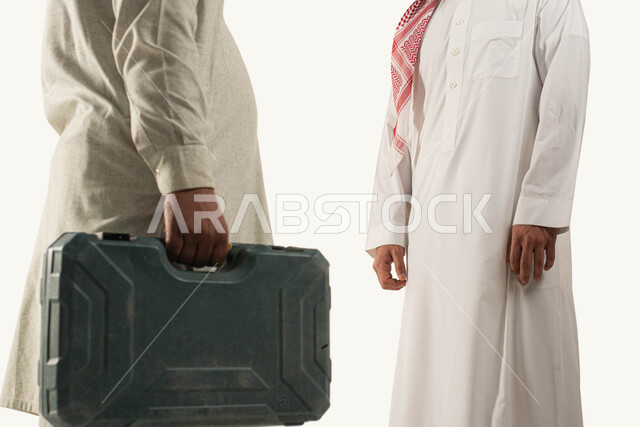 أدوات ومعدات الصيانه, حرف وأعمال تقليدية سعودية, بورتريه لرجل عربي خليجي سعودي يرتدي الثوب التقليدي والشماغ يقف أمام العامل, عامل صيانه يحمل بيديه حقيبة العدة اليدوية, مهن ووظائف سعودية, خلفية بيضاء