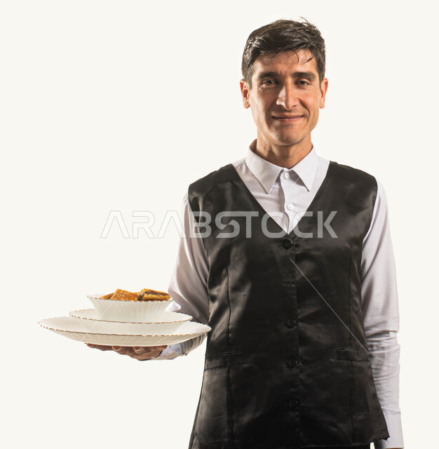 Saudi oriental kitchens and restaurants, varieties of delicious Arabic delicacies, a close-up portrait of a Saudi Gulf Arab waiter wearing a work uniform serving a plate of food, attention and care for customers, looking at the camera with happy gestures, white background