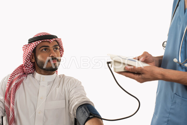 جهاز خاص لقياس ضغط الدم للمرضى, متابعه دورية لإجراء الفحوصات في عيادة خاصه، بورتريه مقرب لرجل عربي خليجي سعودي مبتسم يرتدي الثوب والزي التقليدي يقوم بالاطمئنان على صحته بزيارة الطبيب، التفاؤل في حياة مستقبليه أفضل، خلفية بيضاء