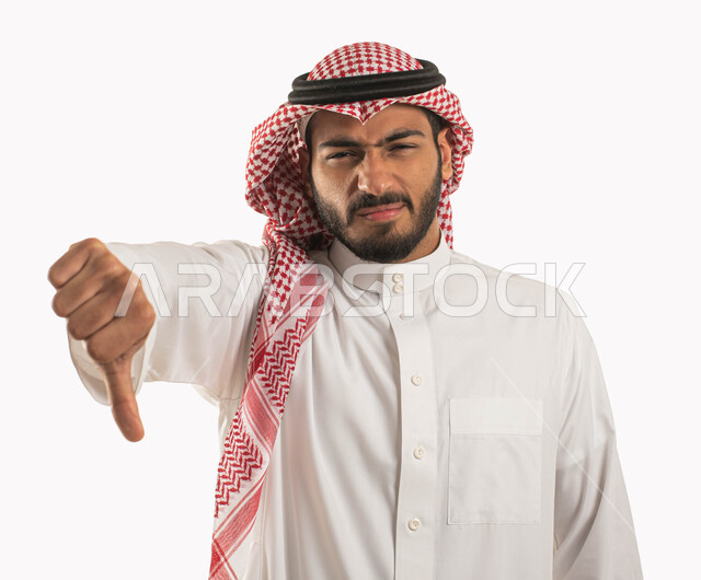 عدم القبول و الرفض و الفشل والخسارة , بورتريه مقرب لرجل عربي خليجي سعودي يرتدي الزي التقليدي والثوب يشير بأصبع الابهام الى الاسفل ، حركات يد تدل على عدم الموافقه و عدم الإعجاب, الشعور بالإنزعاج من شيء ما، خلفية بيضاء