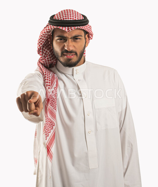 الشعور بالإنزعاج والرغبة بالإنتقام، طلب التوقف عن فعل الأخطاء، حركات يدين تدل على التوبيخ و  الإتهام وإلقاء اللوم، بورتريه مقرب لشاب عربي خليجي سعودي يرتدي الثوب والشماغ التقليدي يرفع اصبع السبابه الى الأمام بغضب وعبوس،  خلفية بيضاء