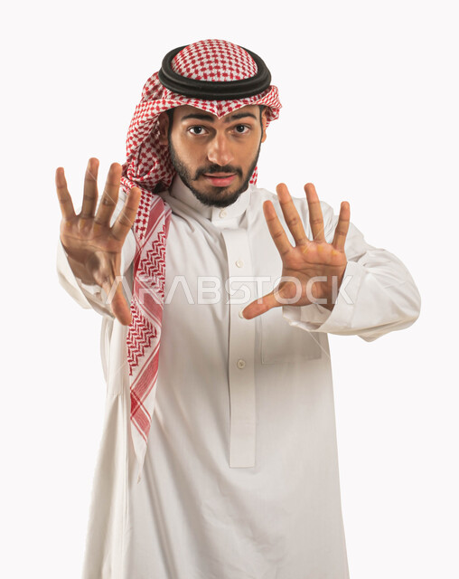 تعابير وإشارات لطلب التوقف والإمتناع عن فعل شيء ما، بورتريه لشاب عربي خليجي سعودي يرتدي الشماغ والثوب التقليدي ويرفع يده للأعلى بإيماءات الخوف والقلق، مفهوم الرعب والذعر و الرهبة، خلفية بيضاء