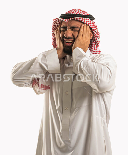التوتر والارهاق وعدم الراحة، بورتريه لرجل عربي سعودي خليجي يرتدي الشماغ والثوب التقليدي ويضع يده على رأسه، إيماءات وجه ويدين تدل على الصداع، الاحساس بألم شديد في الرأس، الاجهاد والضغط النفسي، الشعور بالمرض والحاجة للعلاج، خلفية بيضاء