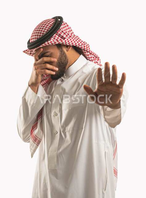 إيماءات الخوف والقلق والانزعاج من أمر ما، بورتريه لرجل عربي خليجي سعودي يرتدي الشماغ والثوب التقليدي ويقوم بتغطية عينه ورفع يده الأخرى لأعلى بإشارة توقف، طلب التوقف والإمتناع عن فعل شيء ما، عدم القبول ورفض الأذى، خلفية بيضاء