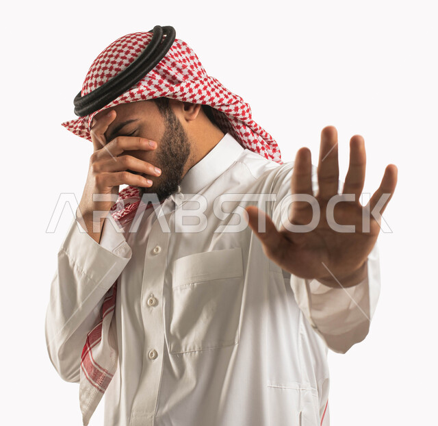 طلب التوقف والإمتناع عن فعل شيء ما، بورتريه لرجل عربي خليجي سعودي يرتدي الشماغ والثوب التقليدي ويقوم بتغطية عينه ورفع يده الأخرى لأعلى بإشارة توقف، إيماءات الخوف والقلق والانزعاج من أمر ما، عدم القبول ورفض الأذى، خلفية بيضاء