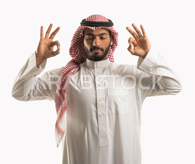 أنشطة وتمارين رياضية، بورتريه لرجل عربي خليجي سعوي يرتدي الثوب التقليدي والشماغ ويغمض عينيه ويرفع يديه إلى أعلى بإيماءات وتعابير التأمل والاسترخاء، ممارسة رياضة اليوغا التأملية، التنفس العميق والتركيز، خلفية بيضاء