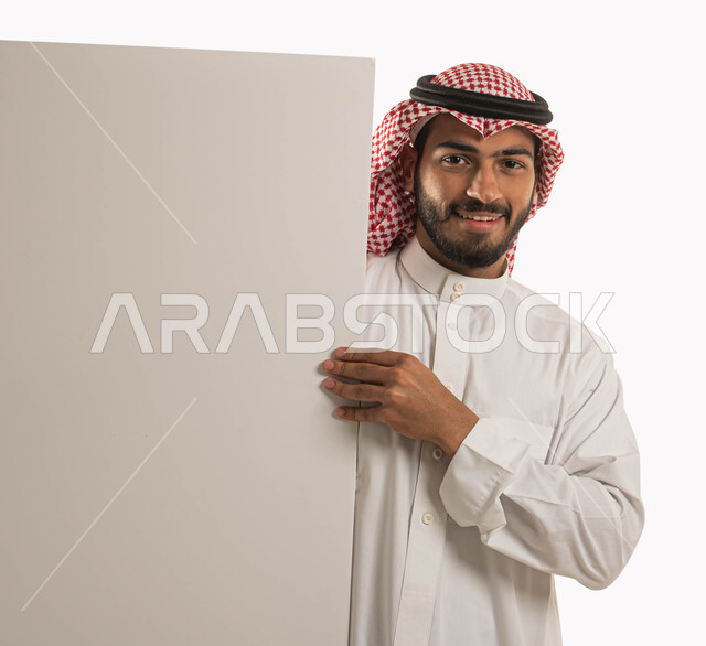 بورتريه لمواطن عربي خليجي سعودي يرتدي الثوب التقليدي والشماغ ويحمل بيده لوح اعلاني فارغ، النظر الى الكاميرا بايماءات السرور والسعادة، عرض الاعلانات والعروض التسويقية، لوحة ورقية فنية تعليمية كبيرة، خلفية بيضاء