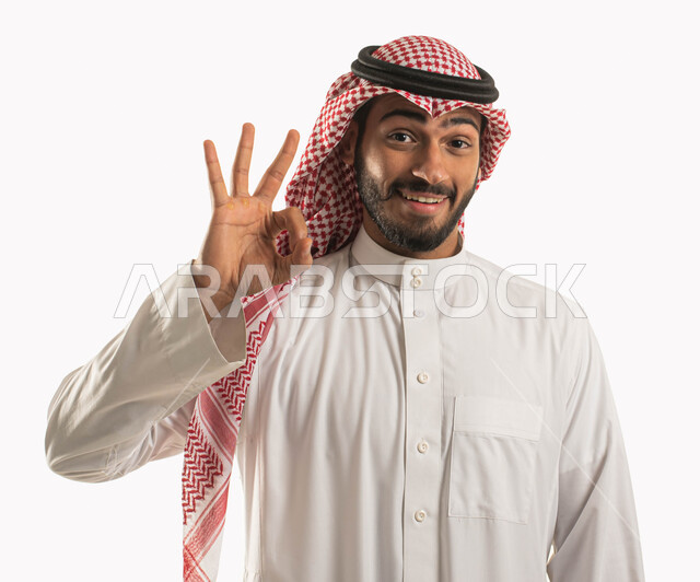 الامتياز والتميز والنجاح، بورتريه لرجل عربي خليجي سعودي يرتدي الثوب التقليدي والشماغ وينظر الى الكاميرا بايماءات السرور والسعادة، رفع اليد بعلامة الجودة، اشارات القبول والموافقة، الاعجاب والرضا بنتجية شيء ما، خلفية بيضاء