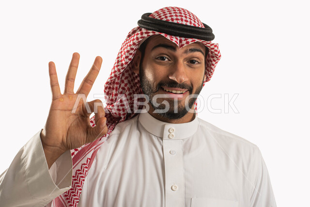 الاعجاب والرضا بنتجية شيء ما، بورتريه لرجل عربي خليجي سعودي يرتدي الثوب التقليدي والشماغ وينظر الى الكاميرا بايماءات السرور والسعادة، رفع اليد بعلامة الجودة، الامتياز والتميز والنجاح، اشارات القبول والموافقة، خلفية بيضاء