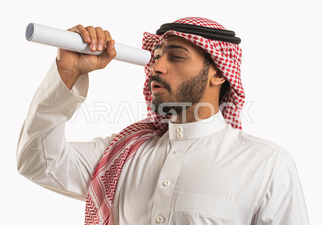 التظاهر باستخدام المايكروسكوب, بورتريه مقرب لرجل عربي سعودي خليجي يرتدي الثوب و الشماغ التقليدي ينظر من خلال ورقة بيضاء ملفوفة, إيماءات الدهشة و الإعجاب, التخطيط للمستقبل البعيد, تقريب الأشياء البعيدة, خلفية بيضاء .