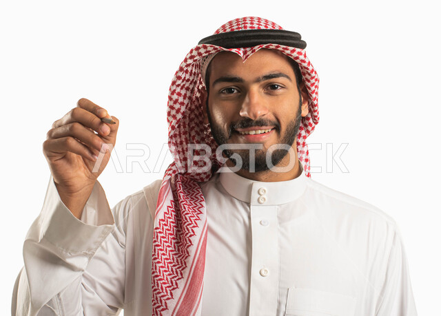 Preparing to write and select something, close-up portrait of a smiling Saudi Arabian Gulf man wearing a traditional thobe and shemagh, hand gestures indicating holding an item, drawing, identifying and pointing, education in the Kingdom of Saudi Arabia, white background.