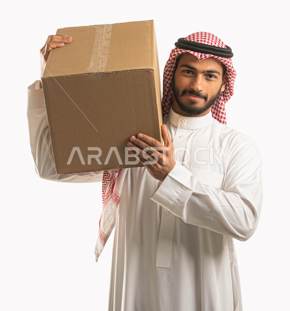 التسوق وطلب المنتجات عبر الإنترنت، عملية توصيل الطلبات للزبائن، خدمات الشحن و التوصيل ذات الجودة العالية، بورتريه مقرب لمندوب عربي سعودي خليجي يرتدي الشماغ والثوب التقليدي ويحمل بيده صندوق كرتوني، خلفية بيضاء