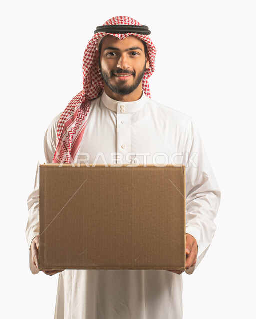 عملية توصيل الطلبات للزبائن، خدمات الشحن و التوصيل ذات الجودة العالية، التسوق وطلب المنتجات عبر الإنترنت، بورتريه مقرب لمندوب عربي سعودي خليجي يرتدي الشماغ والثوب التقليدي ويحمل بيده صندوق كرتوني، خلفية بيضاء