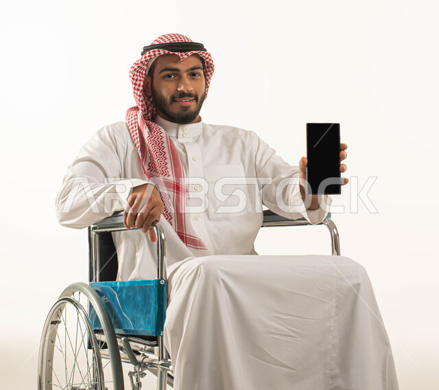 تسهيل حياة ذوي الهمم باستخدام التقنيه والتكنولوجيا, شاشة سوداء فارغه على الهاتف المحمول,  بورتريه لرجل عربي سعودي خليجي  يرتدي الزي التقليدي يقوم بعرض تطبيقات وبرامج ذوي الاحتياجات الخاصه, مريض مقعد يجلس على كرسي متحرك,  ايماءات التفاؤل بالمستقبل, خلفية بيضاء