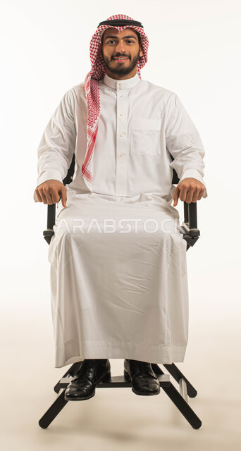 الجلوس على كرسي اسود والنظر الى الكاميرا، صورة شخصية للوثائق الرسمية، بورتريه مقرّب لشاب عربي خليجي سعودي وسيم مبتسم يرتدي الشماغ والثوب التقليدي ويجلس بثقه وطمانينه، الاهتمام بالمظهر الخارجي, وسامة الشباب السعوديين، خلفية بيضاء
