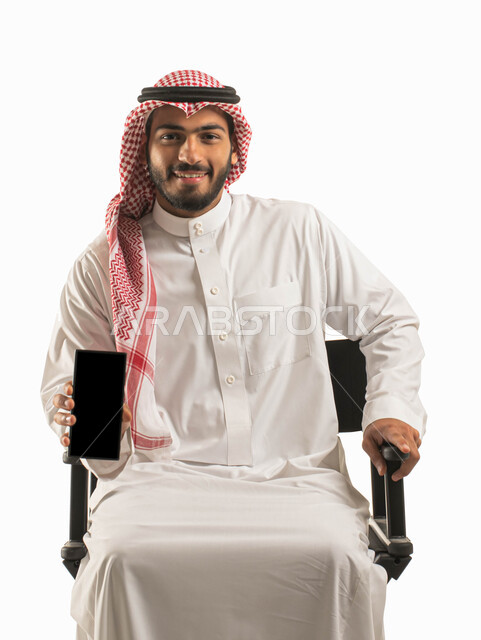 عرض تطبيقات وبرامج الهاتف المحمول، بورتريه لرجل عربي خليجي سعودي مبتسم يرتدي الشماغ والثوب التقليدي يحمل بيده جوال بشاشة سوداء فارغة، الراحه والجلوس على كرسي اسود، ايماءت الاعجاب باستخدام التقنيه والتكنولوجيا الحديثه، مفهوم التسويق الالكتروني، خلفية بيضاء