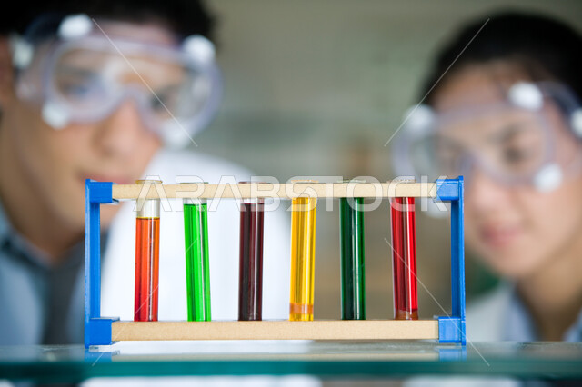 استخدام أنابيب الاختبار لإجراء التجارب في المختبر, صورة مقربة لشاب وفتاة عربيين خليجيين إماراتيين ينظران لأنبوب الاختبار بإيماءات الدقة والتركيز, ارتداء نظارة الوقاية والقيام بتجربة كيميائية, الاستفادة من الأبحاث المخبرية الحديثة